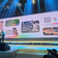 Palestrante em palco durante evento do Google For Brasil 2026, com painel grande exibindo destaques em tela
