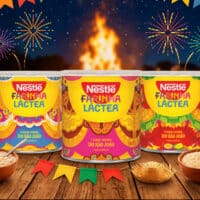 Latas da Farinha Láctea Nestlé em embalagens de Festa Junina, com mesa decorada e fogueira ao fundo.
