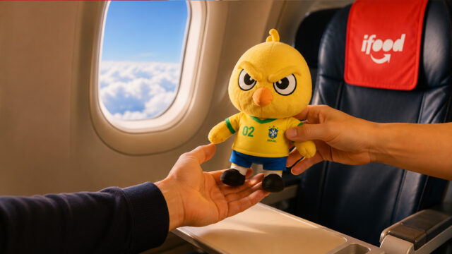 Pássaro Canarinho iFood em mãos dentro de um avião, com janela e banco ao fundo durante ação da Azul