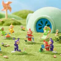 Blind box da coleção Teletubbies da Miniso com miniaturas em cenário lúdico no gramado e caixa ao lado.