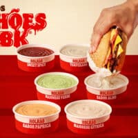 Imagem promocional dos Molhões do BK, com seis potes de molhos do Burger King e uma mão mergulhando um sanduíche