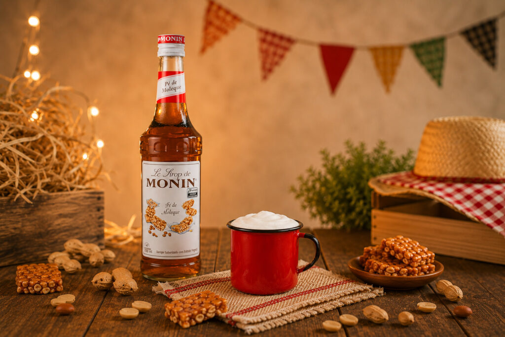 Garrafa de xarope Monin sabor pé de moleque em mesa de Festa Junina, com caneca vermelha e decoração