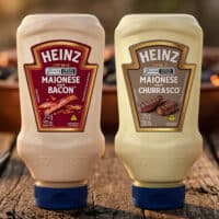 Embalagens de maionese Heinz Bacon e Heinz Churrasco na mesa, com fundo desfocado ao ar livre.