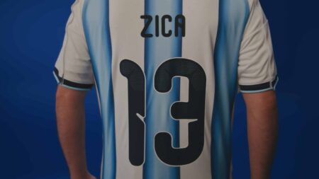 Camisa “ZICA” do Agibank em jogador na Copa do Mundo Jogador de futebol com camisa azul e branca do Agibank, com o texto “ZICA” no centro.
