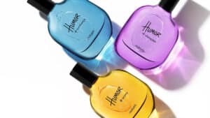 Três frascos da linha Humor da Natura nas cores azul, roxa e amarela, com fragrâncias e rótulos visíveis