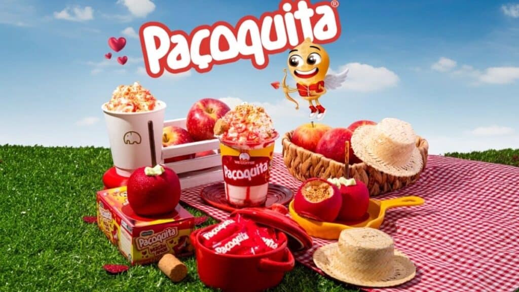 Paçoquita e We Coffee no São João com menu especial Mesa em piquenique com produtos da Paçoquita e xícara da We Coffee, em cenário de São João no campo.
