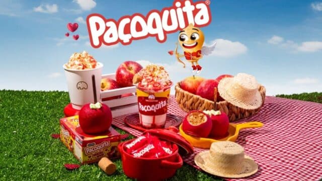Mesa em piquenique com produtos da Paçoquita e xícara da We Coffee, em cenário de São João no campo.