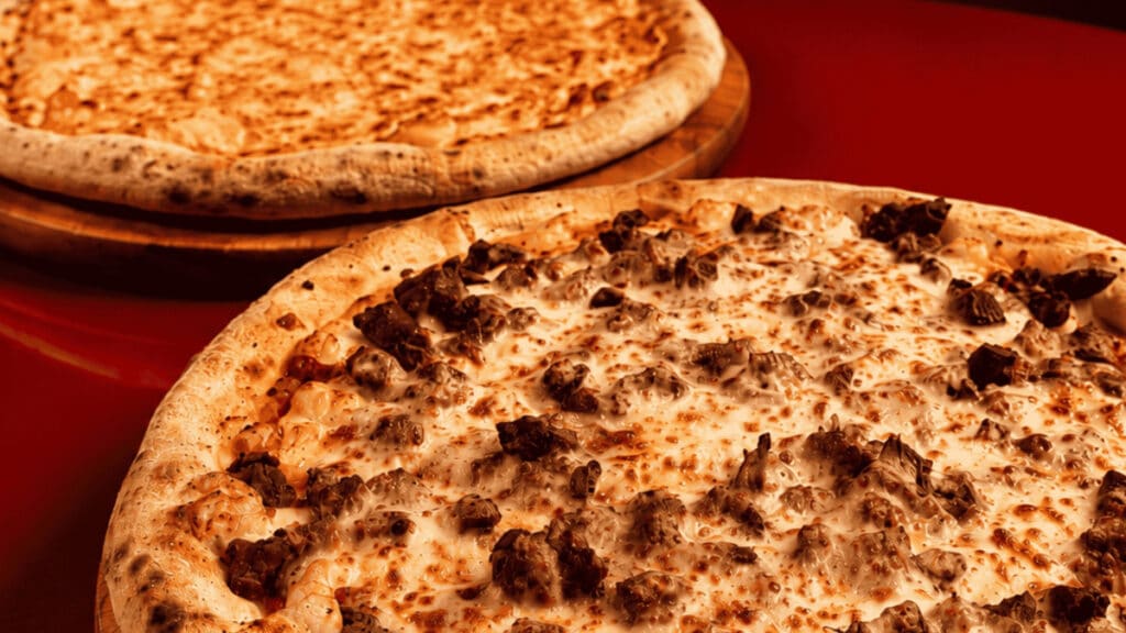 Duas pizzas com cobertura cremosa e pedaços tostados, sugerindo pizza de fondue.