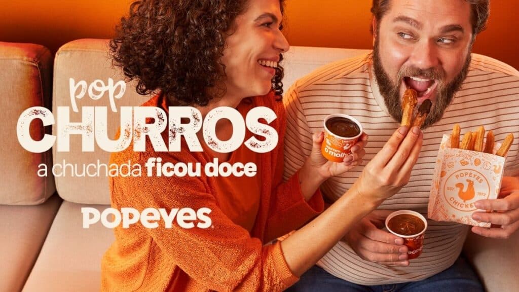 Pop Churros Popeyes: casal prova a sobremesa Casal saboreando Pop Churros do Popeyes, com o produto em destaque e um copo de molho ao lado.