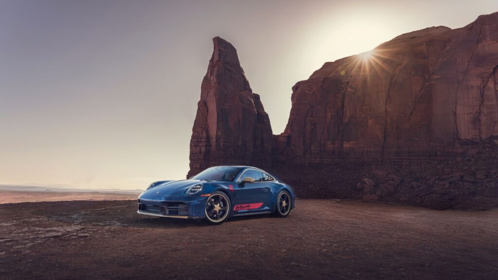 Porsche 911 azul inspirado no Woody, com detalhes estilo Toy Story, em uma estrada de deserto com montanhas ao fundo