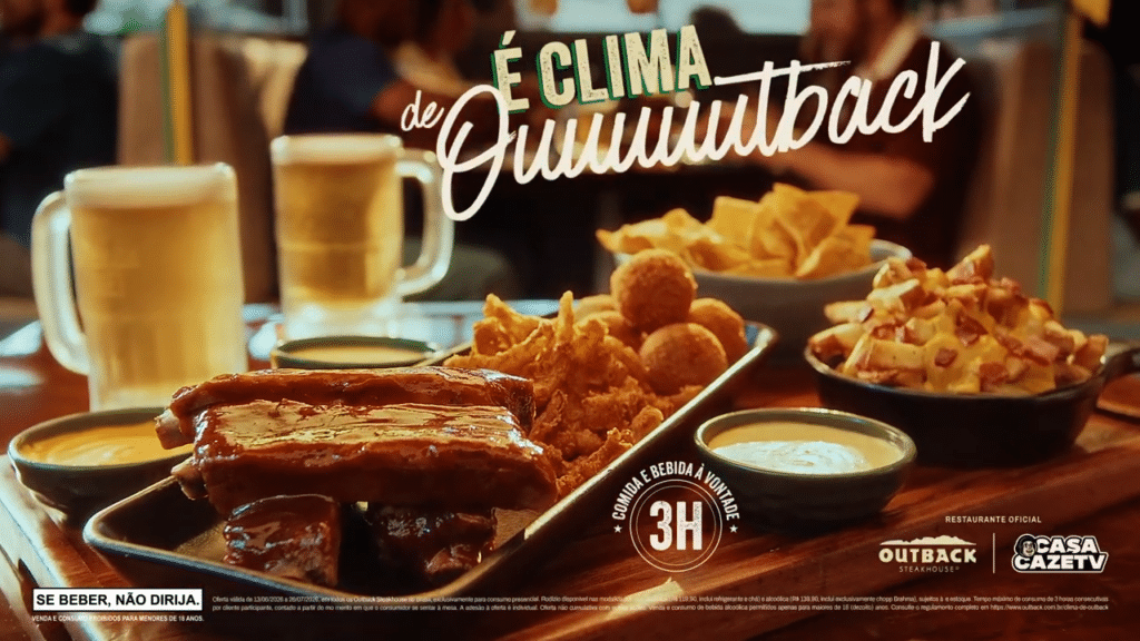 Mesa com porções de comida do Outback, incluindo costela, nuggets e molho, ao lado de canecas de cerveja