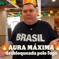 Homem em loja do Burger King, com camiseta “BRASIL” e texto “AURA MÁXIMA”, ao lado de ilustração de chamas da promoção Aura de Fogo.