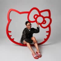 Modelo usando sandálias coloridas em um cenário com logo grande da Hello Kitty em fundo claro