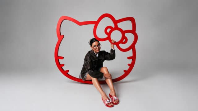 Modelo usando sandálias coloridas em um cenário com logo grande da Hello Kitty em fundo claro