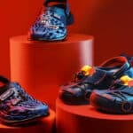 Tênis Crocs em edição Red Bull Racing azul e vermelha sobre suportes laranja, com logotipos visíveis.