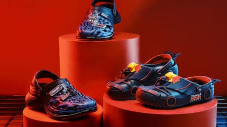 Crocs Red Bull Racing: edição azul e vermelha Tênis Crocs em edição Red Bull Racing azul e vermelha sobre suportes laranja, com logotipos visíveis.