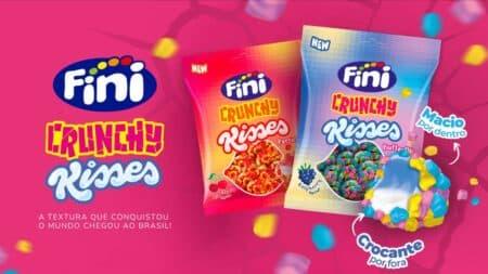 Fini Crunchy Kisses: bala crocante com recheio macio Embalagens de bala Fini Crunchy Risses com textura crocante e recheio macio, no fundo rosa com confetes e a marca Fini