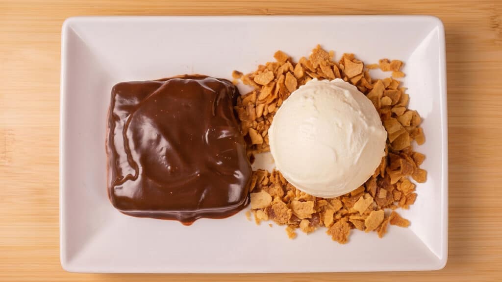 Borelli Torta Al Cioccolato com sorvete Torta Al Cioccolato com cobertura de chocolate e sorvete, servida em prato branco sobre mesa de madeira.