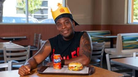 Burger King com Fanta e ator de Kenan & Kel Homem em restaurante do Burger King com chapéu, segurando e ao lado de uma Fanta, com sanduíche em uma mesa