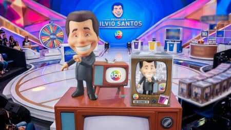 Boneco colecionável Silvio Santos (Silvinho TV) com logo SBT Boneco colecionável do Silvio Santos em uma TV, na bancada do estúdio com o logo do SBT ao fundo.