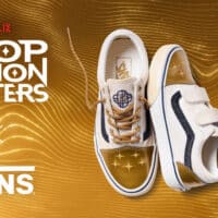 Chuteiras Vans com tema K-Pop Demon Hunters, com logotipo Netflix e texto “K-Pop Demon Hunters” ao fundo em fundo dourado.