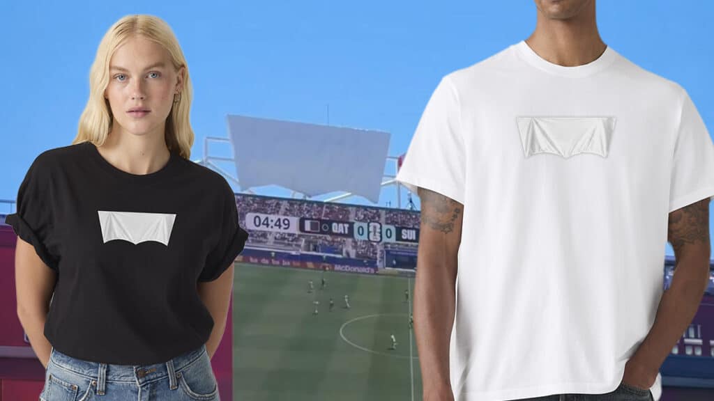 Modelo veste camiseta branca e preta com logo da Levi’s coberto, diante de estádio de futebol em dia de partida da Copa do Mundo.
