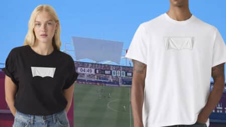Modelo veste camiseta branca e preta com logo da Levi’s coberto, diante de estádio de futebol em dia de partida da Copa do Mundo.