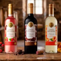 Garrafas Santa Helena Selección à base de vinho em sabores chocolate, frutas vermelhas e pêssego, sobre mesa de madeira.