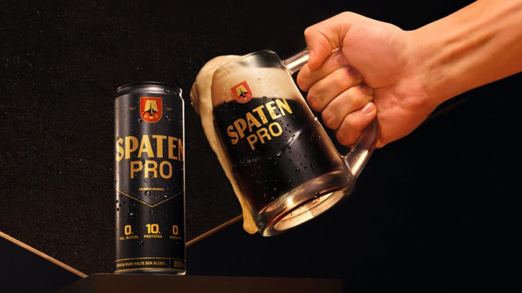 Spaten Pro sem álcool com 10g de proteína Lata e copo de cerveja Spaten Pro sem álcool, com 10g de proteína, sendo servida por uma mão
