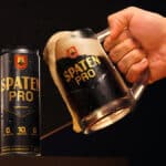 Lata e copo de cerveja Spaten Pro sem álcool, com 10g de proteína, sendo servida por uma mão