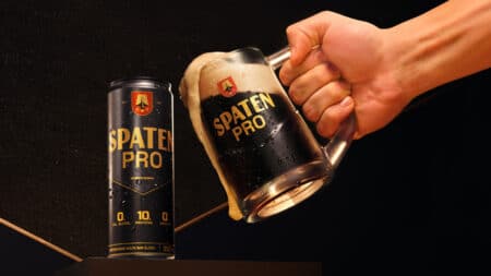 Spaten Pro sem álcool com 10g de proteína Lata e copo de cerveja Spaten Pro sem álcool, com 10g de proteína, sendo servida por uma mão