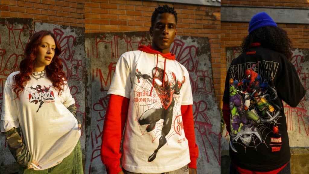 Três pessoas em frente a um muro de grafite usando camisetas com estampa do Homem-Aranha, em um ambiente urbano