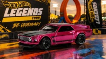 Hot Wheels Legends Tour com carro rosa e banners do evento Carro Hot Wheels Legends Tour rosa em cenário de evento, com banners “Hot Wheels Legends” e “Be Legendary” ao fundo.