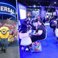 Público em estande da Universal em feira de licenciamento, com personagens Minions e visitantes reunidos no evento