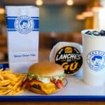 Combo de lanches do Gu com hambúrguer, batatas fritas e copo, em mesa com embalagens da Patties