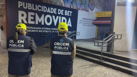 Prefeitura do Rio remove publicidade de bet em espaços públicos Agentes com coletes “Ordem Pública” diante de placa “Publicidade de Bet: Remoção” em área externa do município.