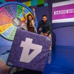 Apresentadores posam em cenário do Quiz&Show, com painel roxo e placa grande de seta no palco