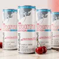 Latas de Red Bull The White Edition Cereja & Baunilha Sugar Free de 250 ml com cerejas ao fundo