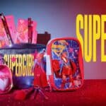 Kit de maquiagem e acessórios “Supergirl” da Miss Frandy, com necessaire rosa e produtos sobre fundo vermelho e azul.