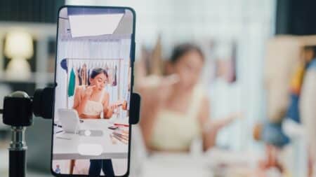 Vlogger gravando no celular com microfone em destaque Close-up de celular gravando vídeo de mulher vlogger em tela, com microfone ao fundo, em ambiente interno