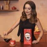 Sandy posa com uma embalagem do Café União em cenário de cozinha, preparando a bebida