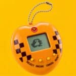 Tamagotchi exclusivo 3 Corações no Rock in Rio 2026, com tela e botões em design amarelo e xadrez