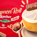 Cinnamon roll Loacker da Bakebun com cobertura cremosa e pedaços de chocolate ao fundo vermelho, em promoção.