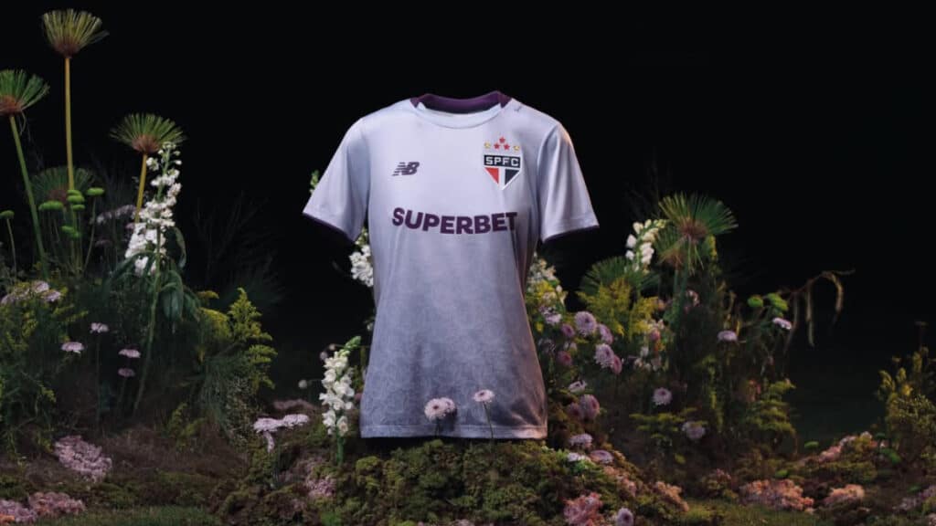 Camiseta do São Paulo feminina branca em fundo de jardim com flores, destaque para escudo e patrocinador no peito.