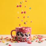 Caneca colecionável do Cartoon Network com personagens, sobre mesa com confetes coloridos em fundo amarelo.