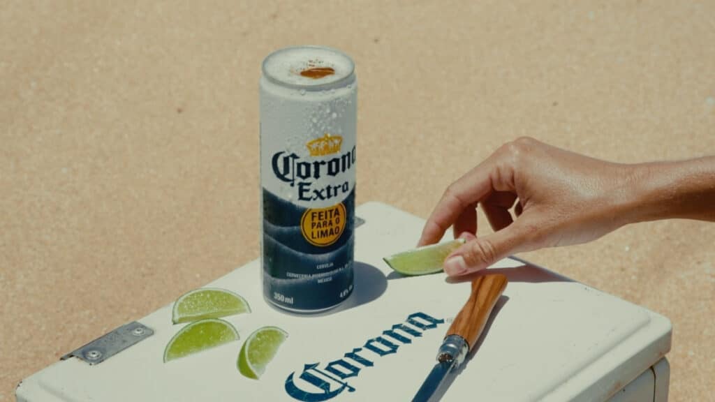 Lata de Corona Extra com tampa aberta e mão preparando fatia de limão sobre superfície branca