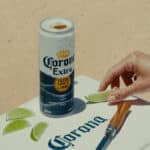 Lata de Corona Extra com tampa aberta e mão preparando fatia de limão sobre superfície branca