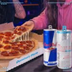 Mesa com pizza da Domino’s e latas de Red Bull, em parceria promocional.