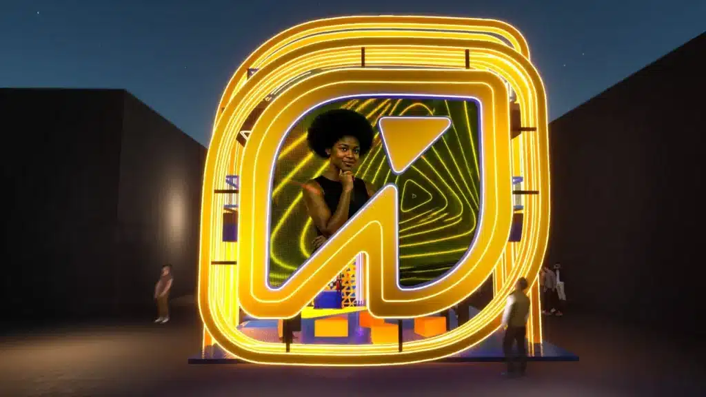 Imagem com letreiro luminoso estilo marca, no cenário de evento do Rock in Rio 2026, com pessoas ao fundo.