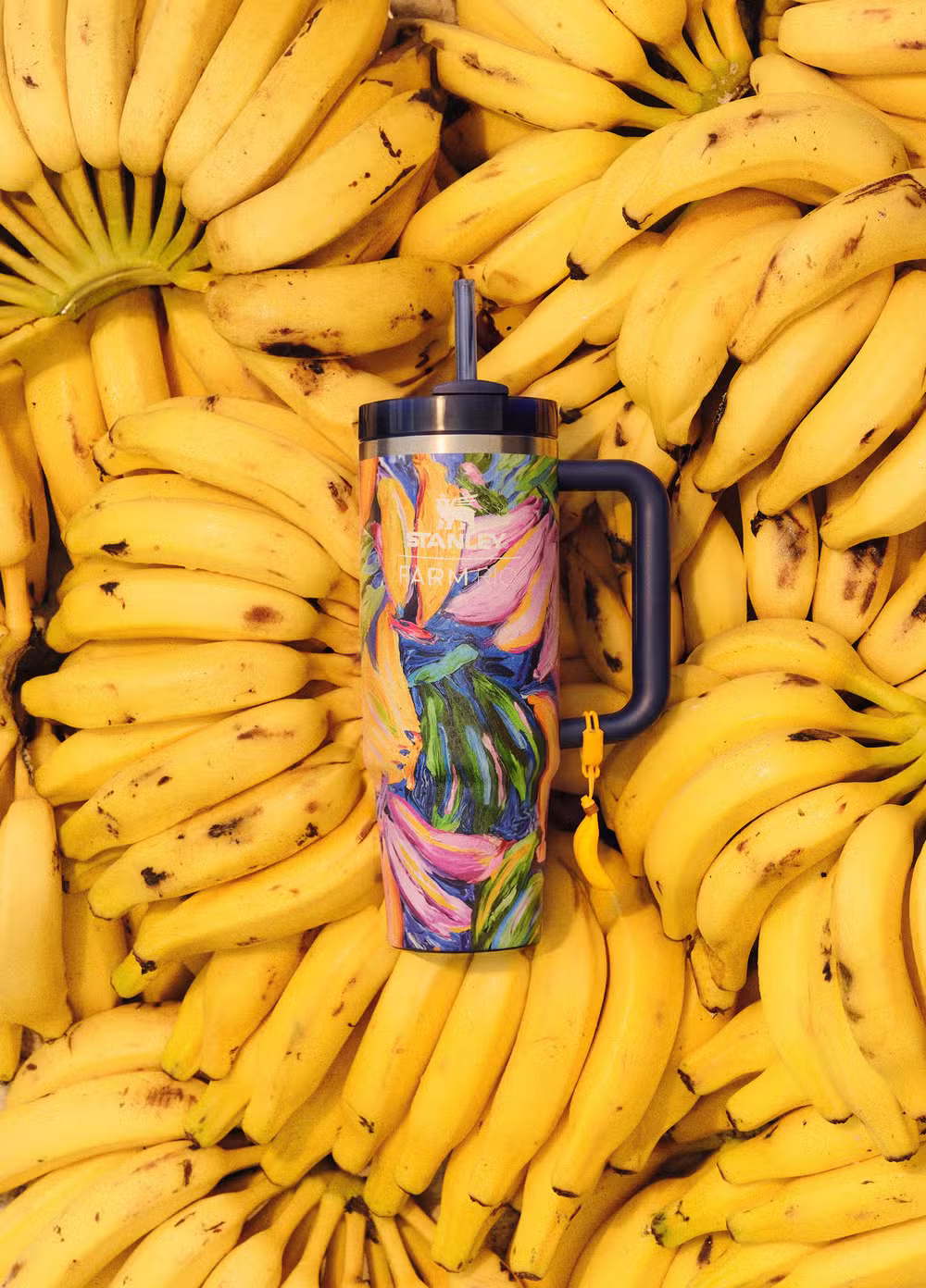 Copo térmico Stanley com estampa colorida e tampa, em meio a bananas maduras